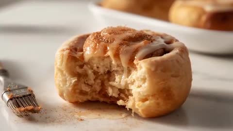 Close-up Bite Revealing Soft Crumb of Glazed Cinnamon Roll Being Brushed with Icing