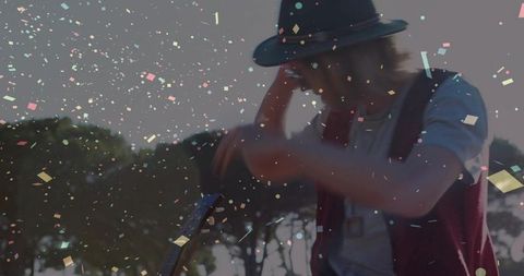 Bohemian musician playing acoustic guitar in park with confetti at golden hour