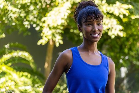 African woman smiling in sunlit garden wearing cobalt blue tank top with bun and summer style