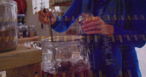 Stirring homemade preserves in large glass jar while holding small jar and spoon