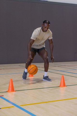 African american athlete dribbling basketball through cones on indoor gym hardwood court