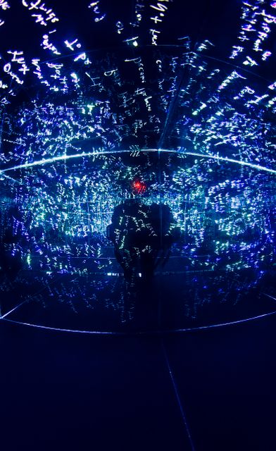 Person standing in a dark room filled with blue glowing data projections on walls and floor, creating a high-tech, futuristic feel. Ideal for illustrating technology, digital innovation, virtual reality, cybersecurity, or an immersive multimedia experience. Perfect for use in presentations, articles, social media posts, and brochures related to tech advancements and modern digital environments.