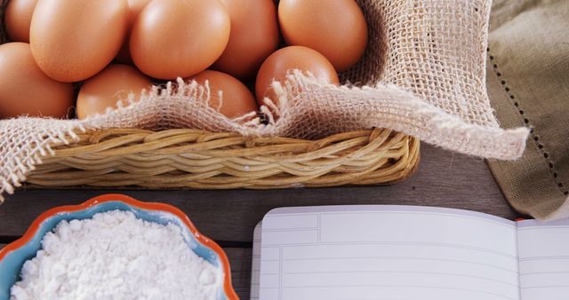 Eggs arranged in a woven basket, a bowl of flour, and an open recipe book on a wooden surface conveys the onset of a home baking session. Ideal for use in food blogs, cooking tutorials, and recipe websites.