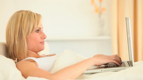 Woman Relaxing While Using Laptop on Bed