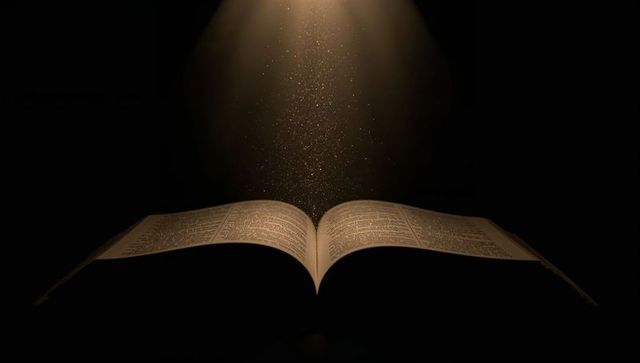 Glowing open book under spotlight with golden dust particles conveying magic and wisdom
