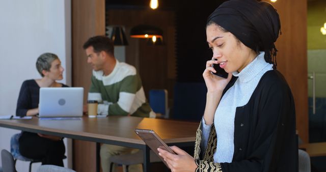 Businesswoman in Hijab Talking on Phone Holding Tablet in Modern Office - Download Free Stock Images Pikwizard.com