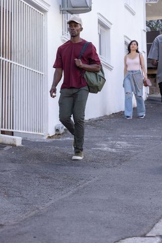 Man walking with duffel bag and cap in urban alley, candid street lifestyle