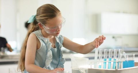 Young student wearing safety goggles conducting chemistry experiment with test tubes