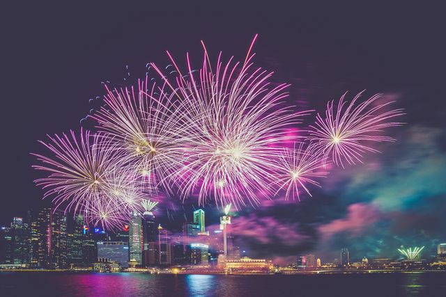 Bright colorful fireworks explosion over urban cityscape with illuminated buildings at night. Great for New Year celebrations, festive events, promotional materials or party invitations emphasizing joyous occasions. Ideal for conveying themes of celebration, festivity, and nighttime city events.