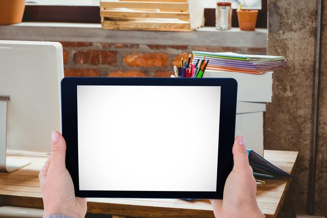 Person holding tablet with blank screen in modern office. Ideal for demonstrating applications, websites, or digital content in professional settings. Can be used for advertising technology products, promoting office setups, or highlighting digital tools.