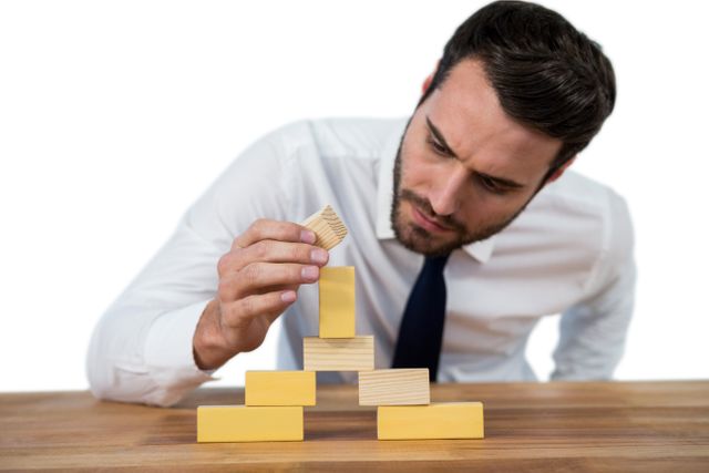 Businessman carefully placing wooden block on a tower, representing strategic planning and problem-solving in a business context. Ideal for use in articles or presentations about leadership, teamwork, business strategy, and creative thinking.