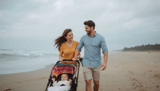 Young couple walking beach pushing baby in stroller during overcast day