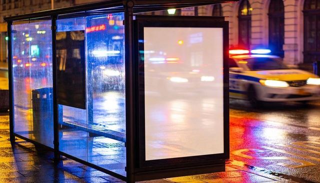 Blank lightbox at rainy city bus stop reflecting police lights for ad mockups