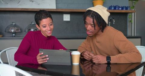 Diverse friends sharing tablet and coffee while collaborating at modern cafe