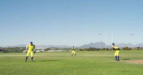 Three cricketers fielding on sunny outfield wearing high-visibility yellow uniforms and gloves