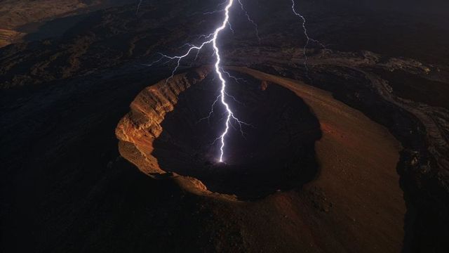 Lightning striking volcanic caldera at night illuminating terraced crater walls and plume