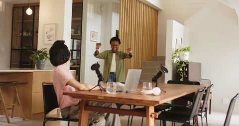 Energetic co-host celebrating during home podcast recording in modern open-plan dining