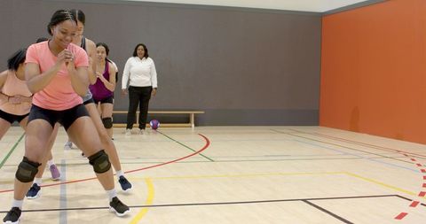 Female team performing squat drill in indoor gym with coach overseeing training
