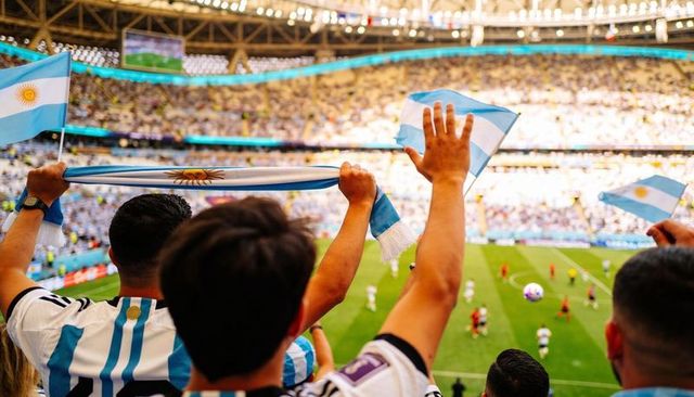 Argentina fans cheering in packed stadium waving flags and lifting scarf