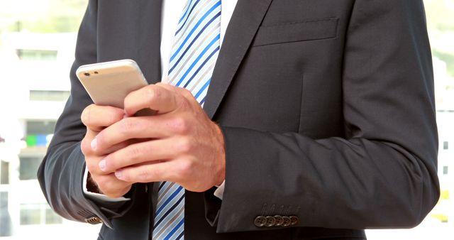 A Caucasian businessman in a suit is focused on his smartphone, with copy space. His attire and engagement with the device suggest a professional setting, dealing with work-related communications.