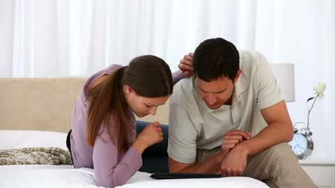Couple Relaxing on Bed Using Tablet Together