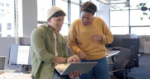 Diverse coworkers collaborating on laptop with charts and analytics in modern open office