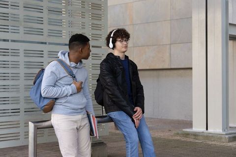 Diverse teenage students leaning on campus rail, chatting while holding notebooks and backpacks