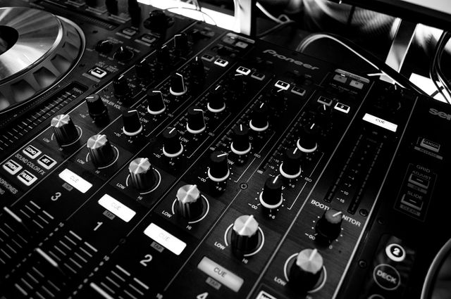 A close-up view of a DJ mixer console with various buttons and knobs captured in black and white. Ideal for use in articles, promotional materials, or designs related to music production, DJ events, parties, and sound engineering.