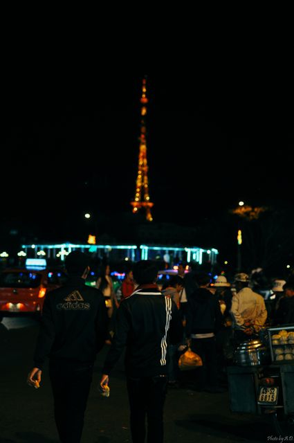 Two Men Walking Through Night Market with Illuminated Tower Background - Download Free Stock Images Pikwizard.com