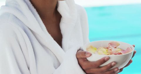 Woman in white robe holding bowl of petals by poolside