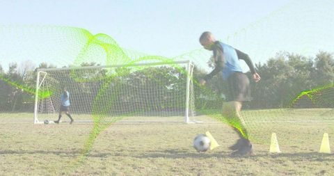 Male soccer player dribbling through cones on grass field with portable goal and teammate