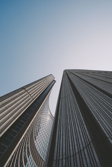 This image showcases two tall skyscrapers with a modern architectural design, captured from a low angle looking up towards the sky. Ideal for use in real estate, urban development presentations, architectural magazines, or promotional materials highlighting cityscapes and modern infrastructure.