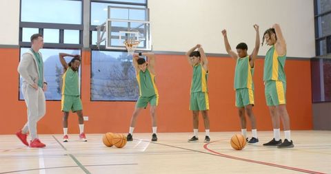 Basketball Team Stretching with Coach on Indoor Court