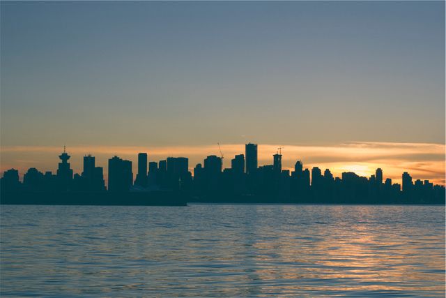 The image captures the elegant silhouette of an urban skyline against a vibrant sunset backdrop, with the city reflecting in the tranquil waters below. Perfect for use in tourism materials, architectural promotions, urban lifestyle content, or as a calming background for digital projects.