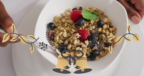 Hands presenting bowl of granola with berries and mint, festive gold bells overlay