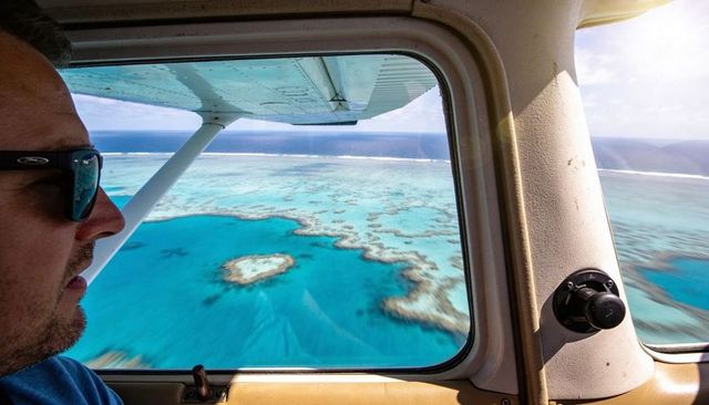 Gazing traveler observing turquoise coral reef from plane window over tropical lagoon