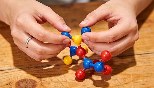 Adult hands assembling colorful ball-and-rod molecular model on wooden table close-up stem