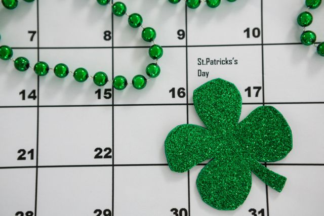 Perfect for illustrating St. Patrick's Day celebrations, this image features a glittery green shamrock and green beads placed on a calendar. Ideal for use in holiday promotions, event planning, social media posts, and festive decorations.