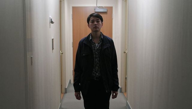Young man standing in dim corridor facing camera, moody low light portrait with centered composition