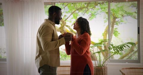 Sunlit couple holding hands by sliding door with woven planter, intimate home romance