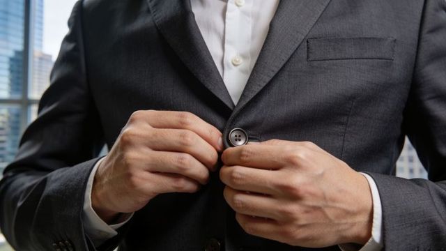 Businessman fastening middle button on charcoal suit jacket, corporate style closeup