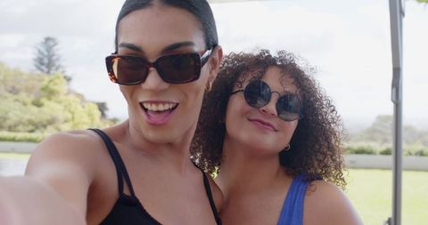 Two african american women taking selfie on sunny patio smiling friends wearing sunglasses
