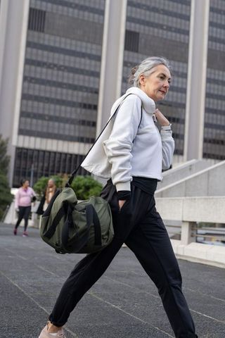 Mature woman walking with duffel bag tapping smartwatch during urban commute