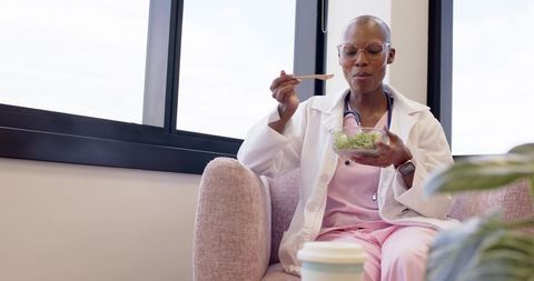 African american nurse eating salad during break in bright medical lounge