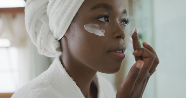 Portrait of african american attractive woman applying face cream in bathroom. beauty, pampering, home spa and wellbeing concept.
