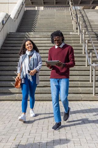 Diverse young professionals walking down plaza steps using tablet and smartphone