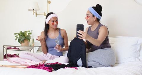 Two friends enjoying pajama party trying on loungewear and sharing skincare pampering