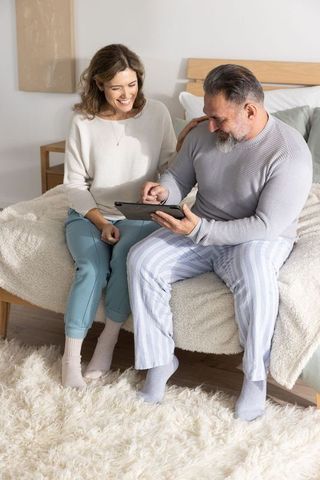 Mature couple relaxing in bed using tablet together, sharing laughter and planning morning