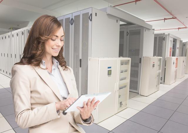 Businesswoman holding digital tablet while working in a server room. Suitable for technology, IT infrastructure, cloud computing, cybersecurity, and professional workplace themes. Ideal for use in websites, tech blogs, magazines, and corporate training materials emphasizing the role of technology in modern business.