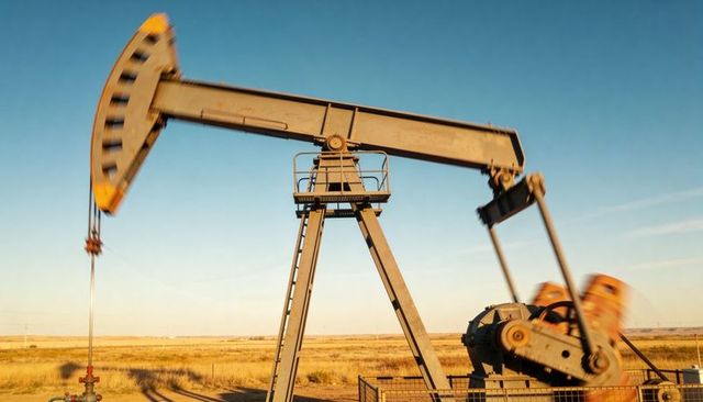 Rusty pumpjack pumping crude on prairie well pad with walking beam and ladder at dusk